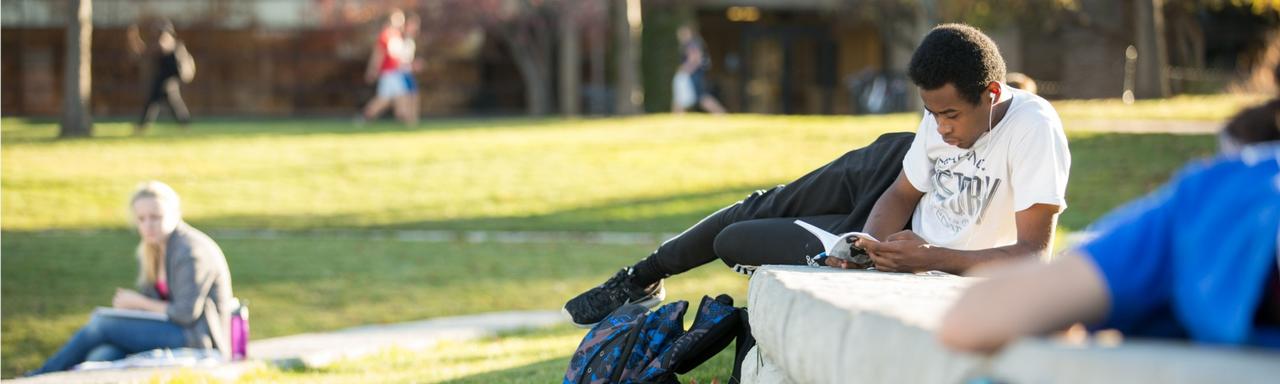 student laying on a wall reading a book outside